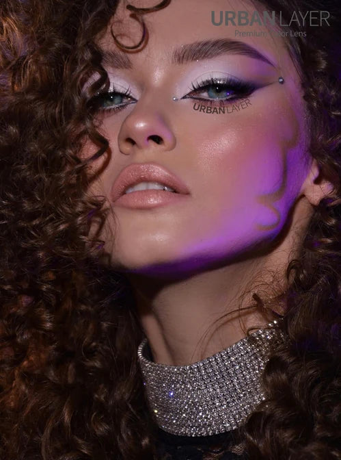 Close-up of a person with curly hair and purple makeup, wearing a sparkling silver earring.