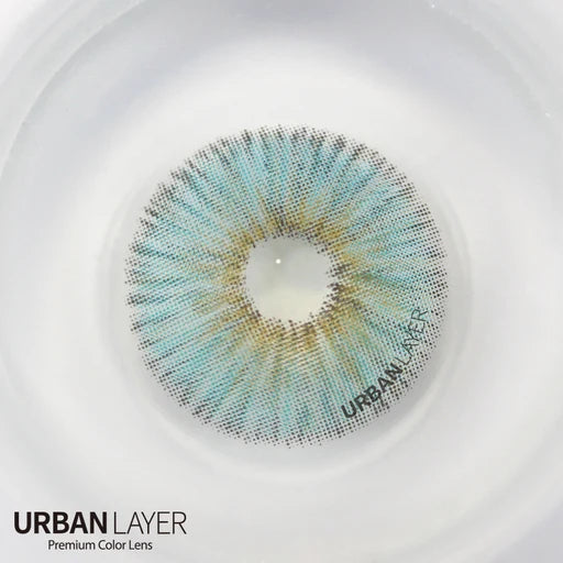 A close-up of a single contact lens with a blue-green and gold gradient pattern, labeled 'URBAN LAYER', set against a white circular background with the text 'URBAN LAYER Premium Color Lens' at the bottom left.